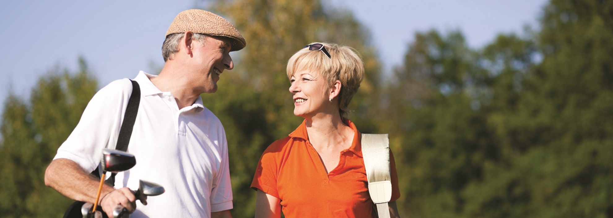 Couple smiling at each other carrying golf clubs
